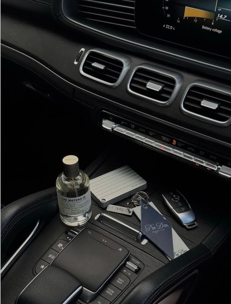 Fragrance bottle and travel essentials on the console of a luxury car interior